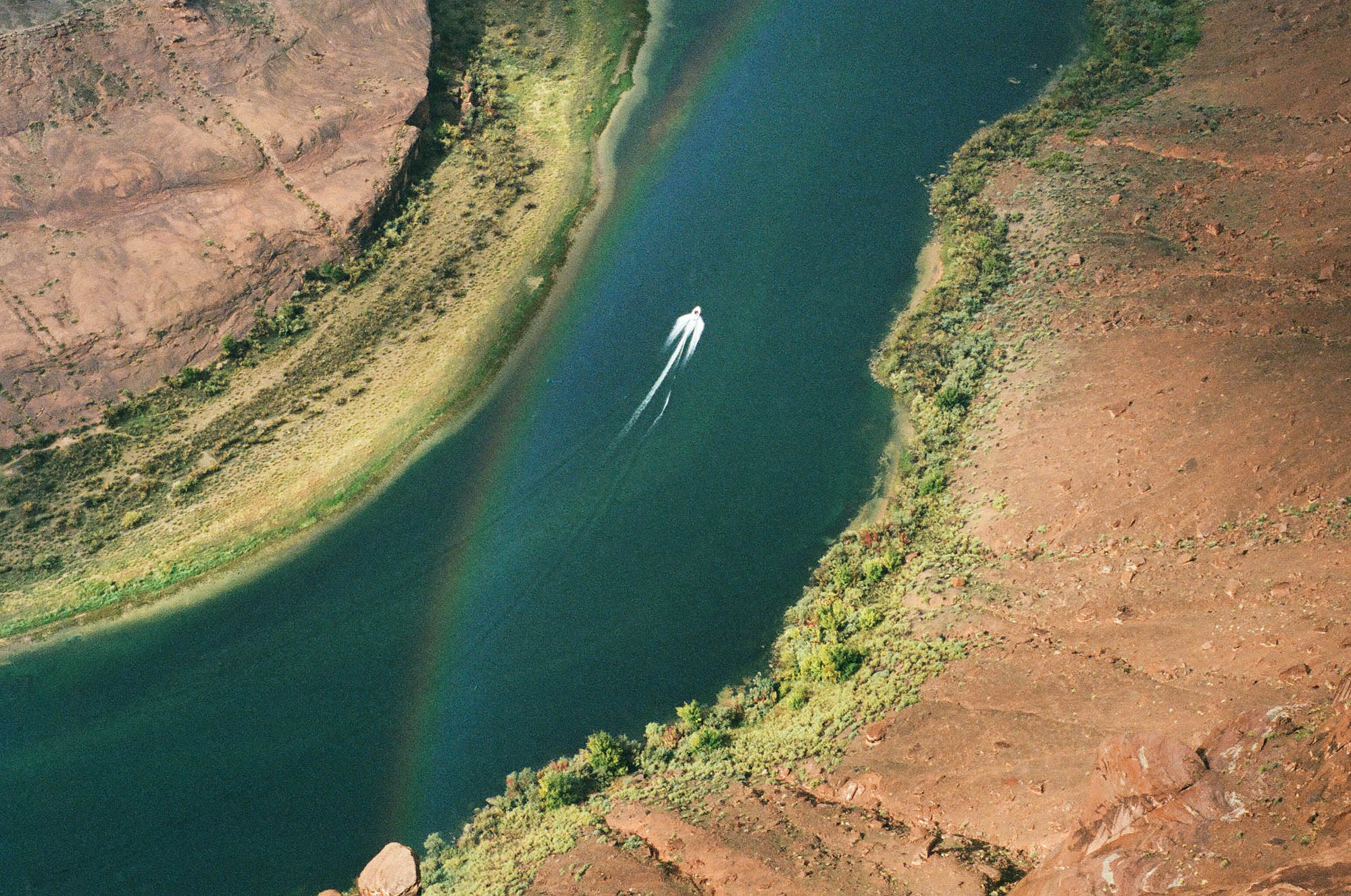 A boat on the Colorado river from above, with a rainbow in the foregeound