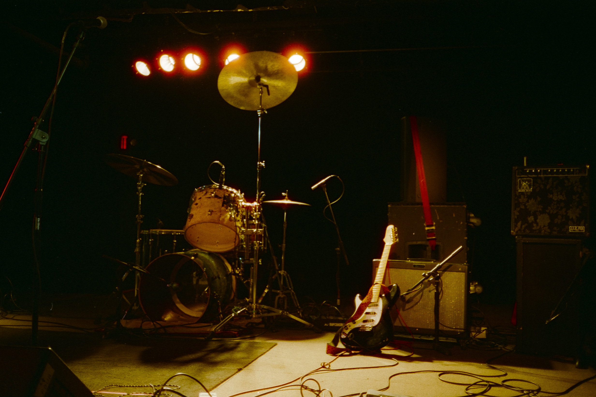 A drum kit, guitar, and amps on an empty stage