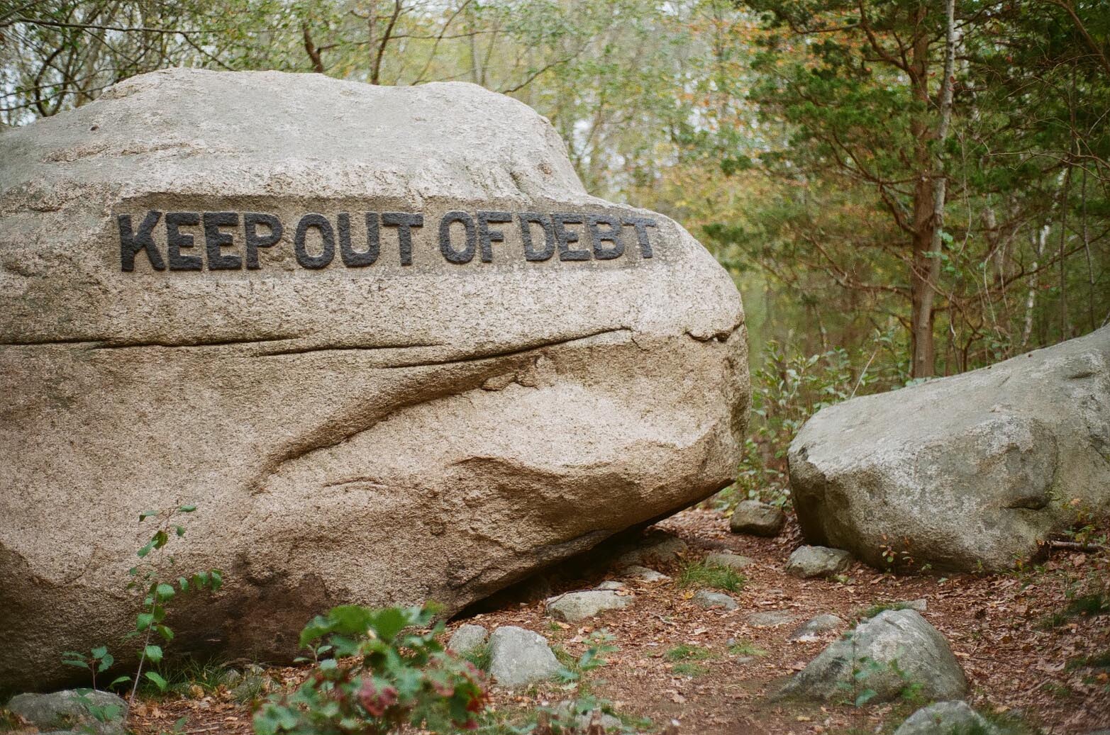 A boulder in the woods carved with the phrase: Keep Out Of Debt