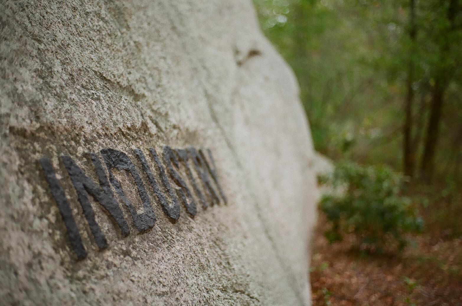 A boulder in the woods carved with the phrase: Industry