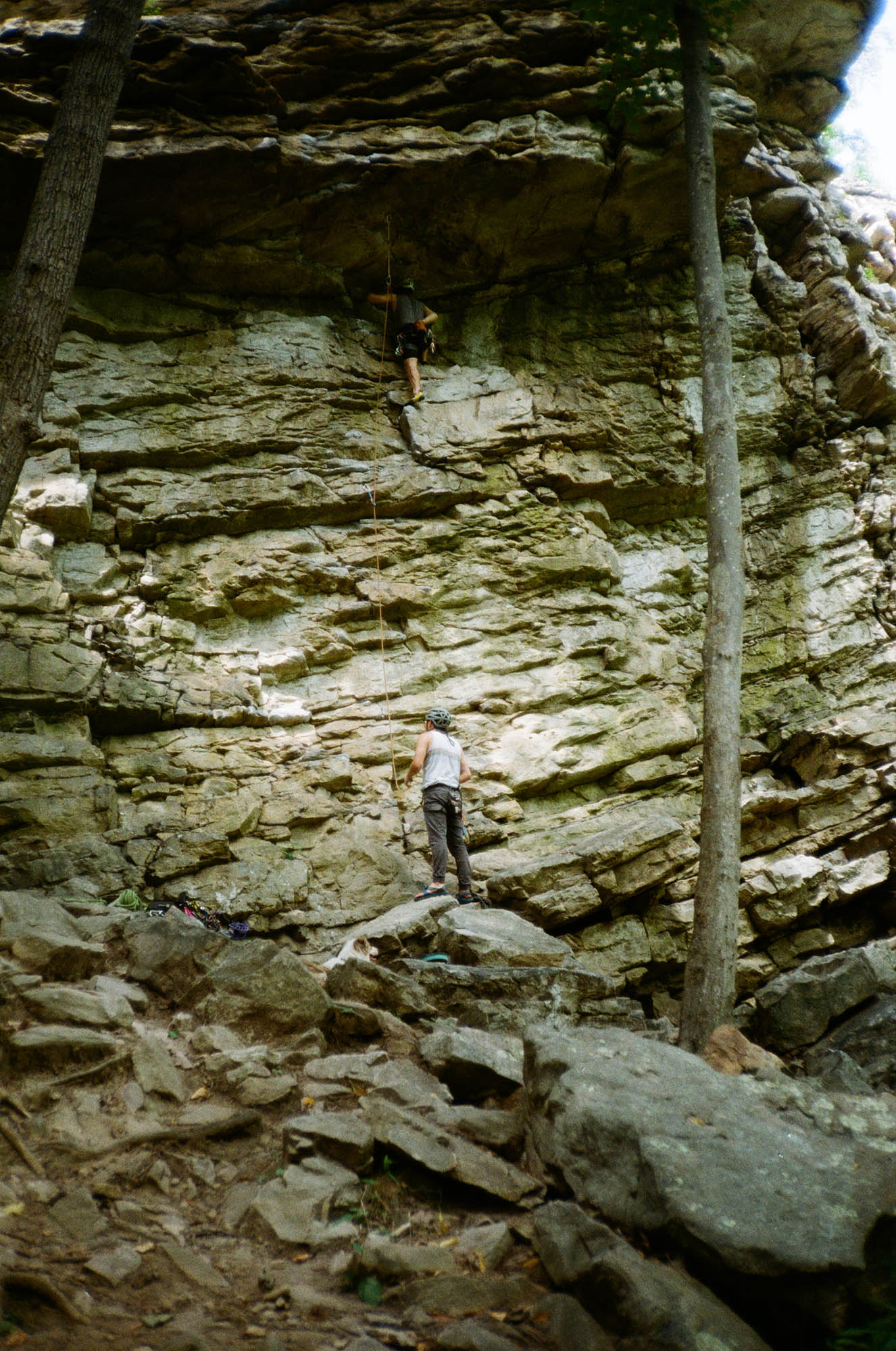 A tall rock wall in the woods with two people climbing