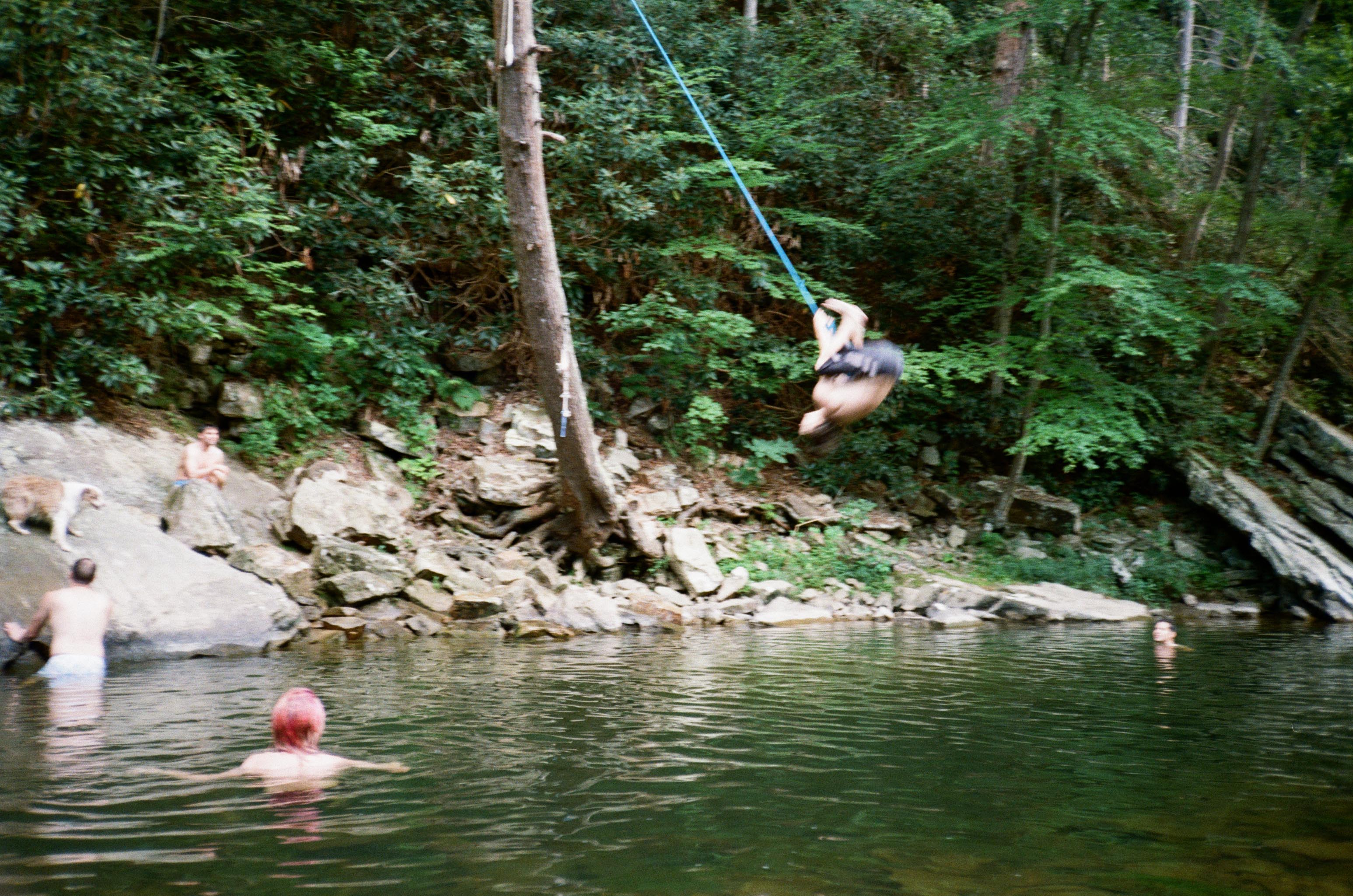A person mid-backflip off a rope swing into a river