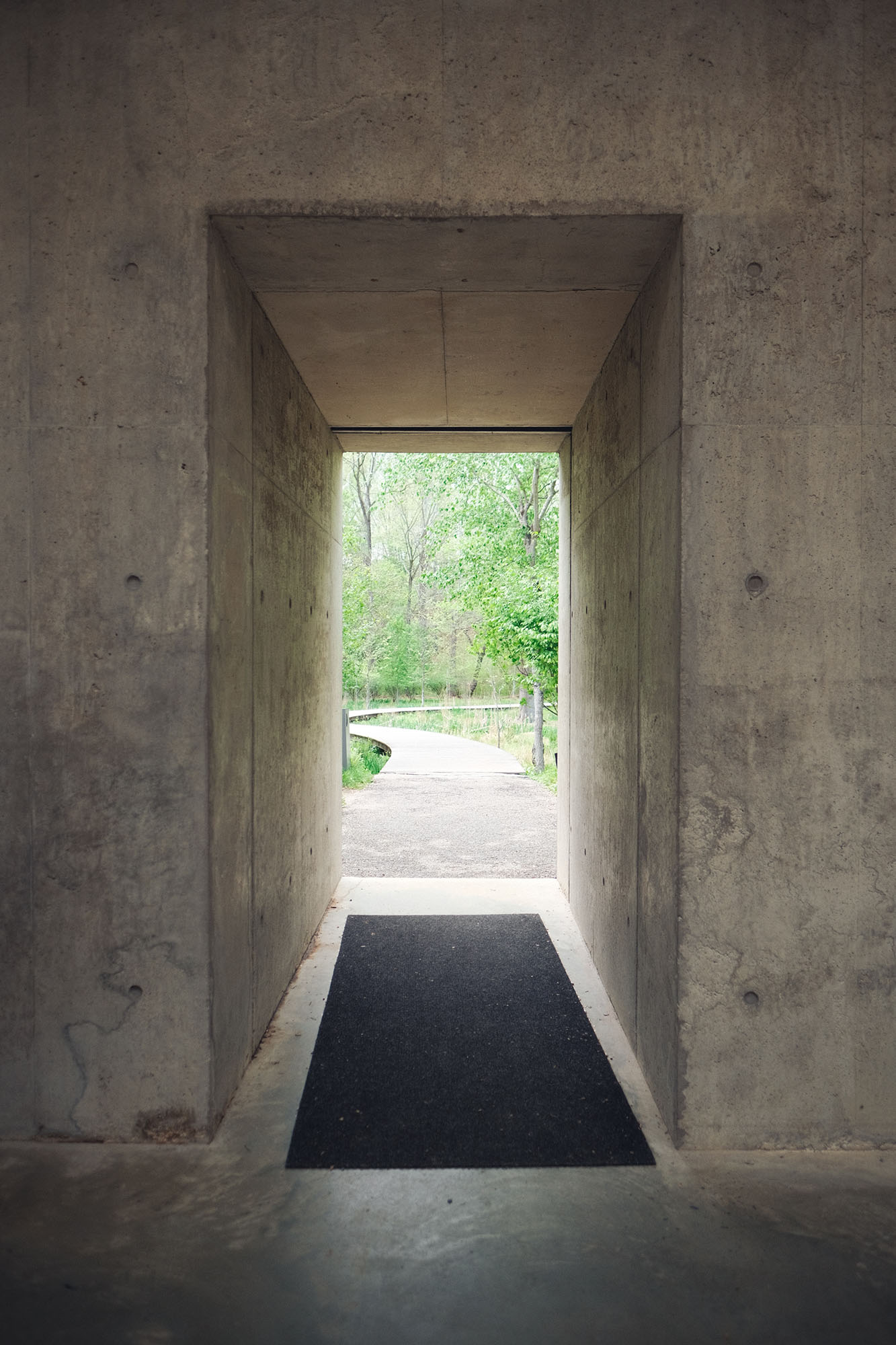 A rectangular opening in a thick concrete wall looking out to the woods
