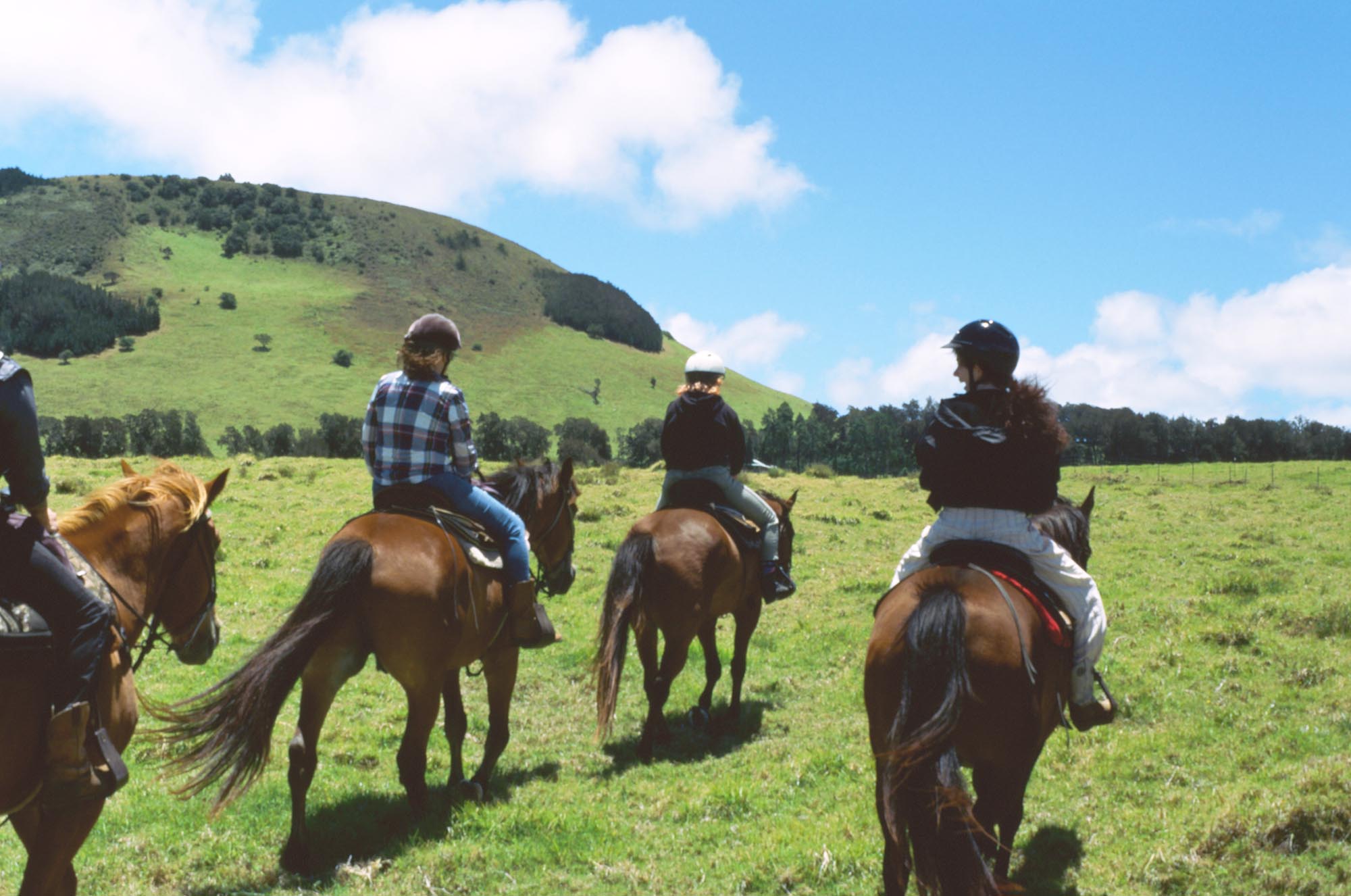 A group of people riding horses up a wide open field