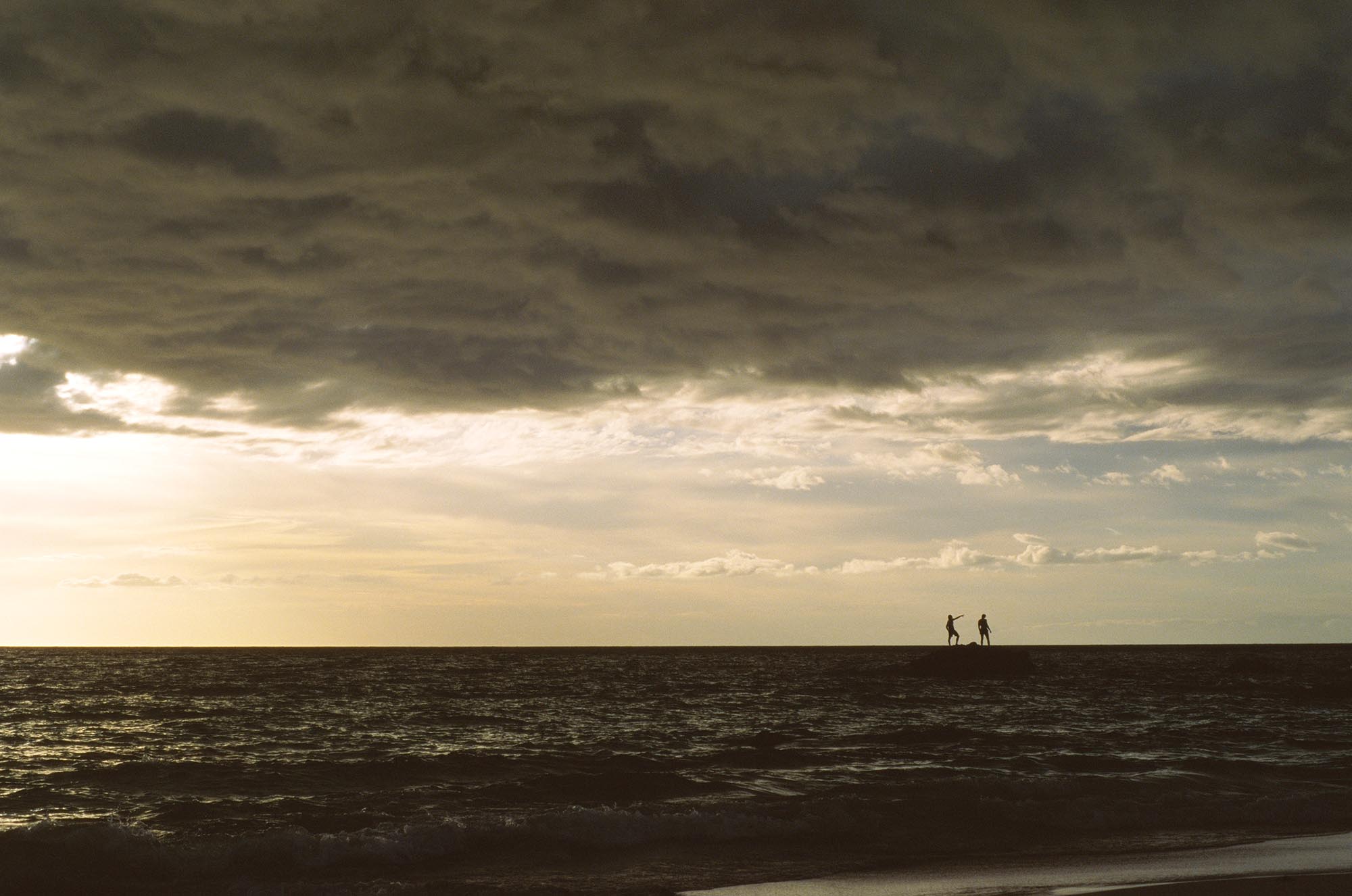 Two small silhouettes on a rock in the middle of the ocean