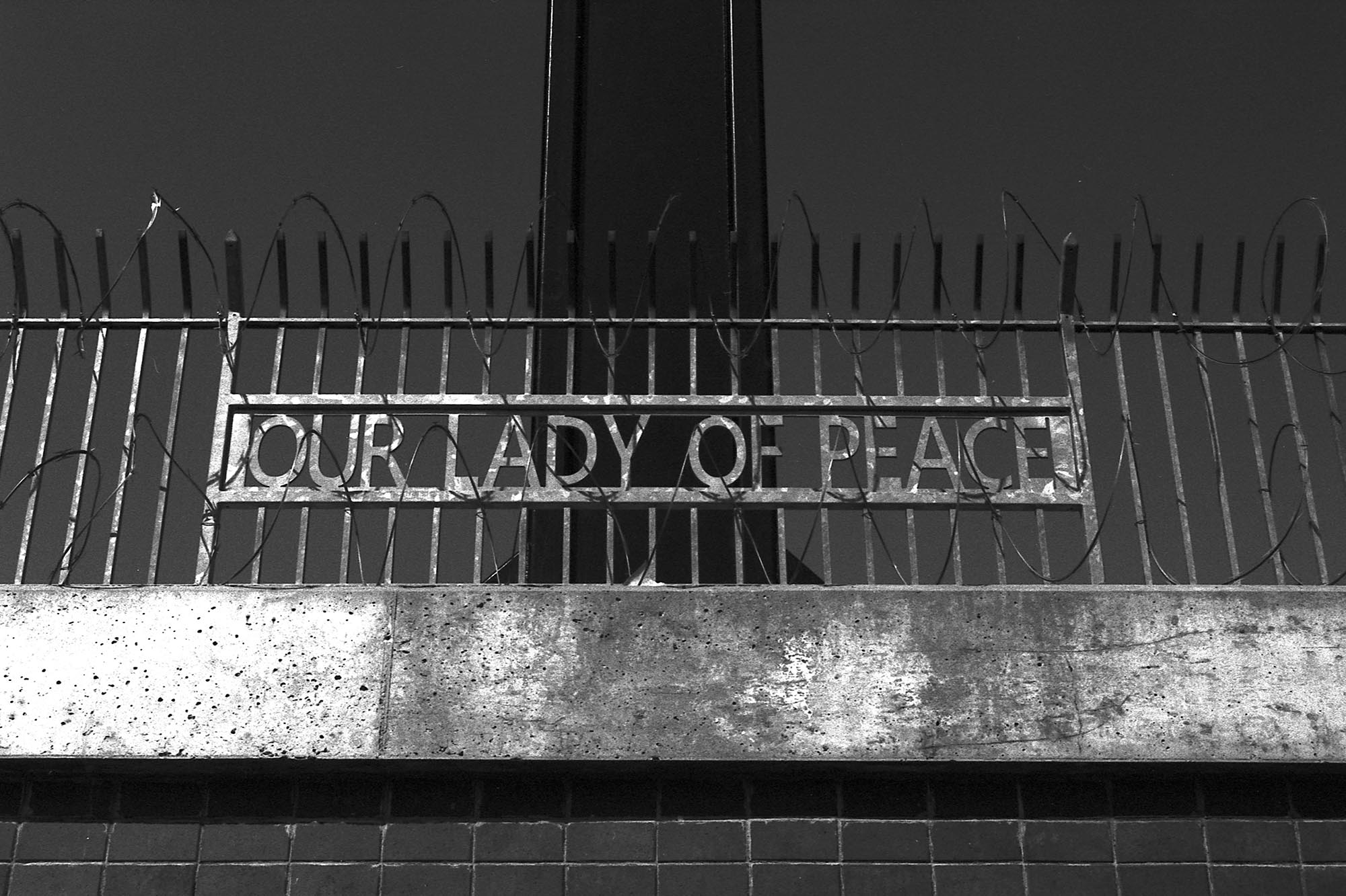 A metal fence with the words Our Lady of Peace wrapped in barbed wire