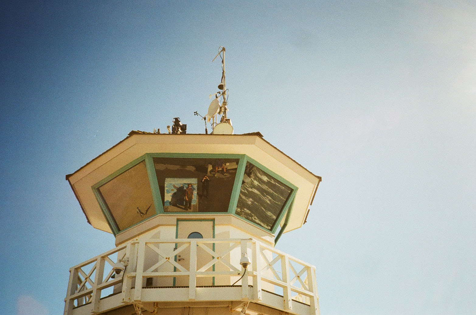 The top of a watchtower at Huntington Beach, people's reflections seen in the windows