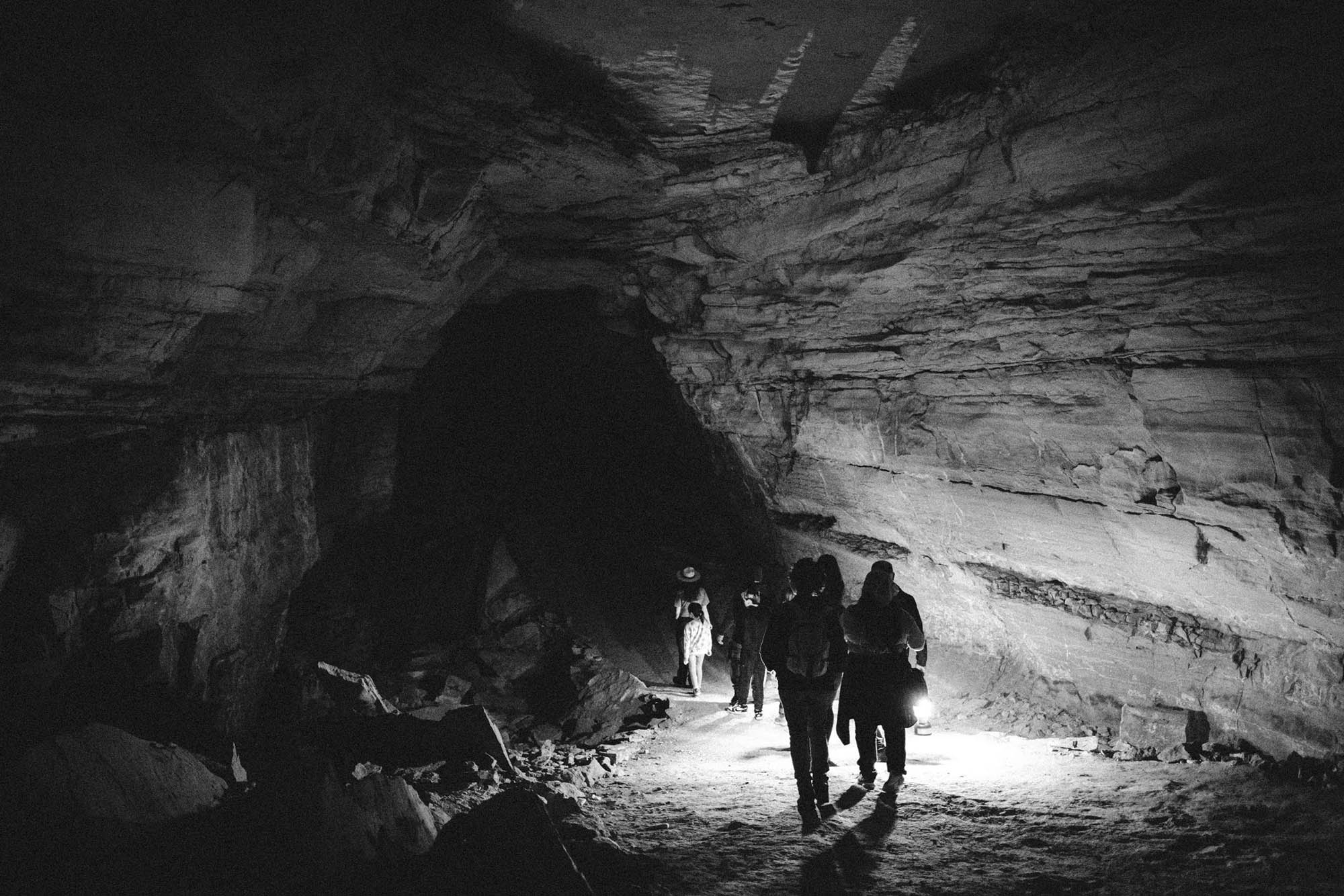 Silhouettes holding lanterns walking into a dark cave