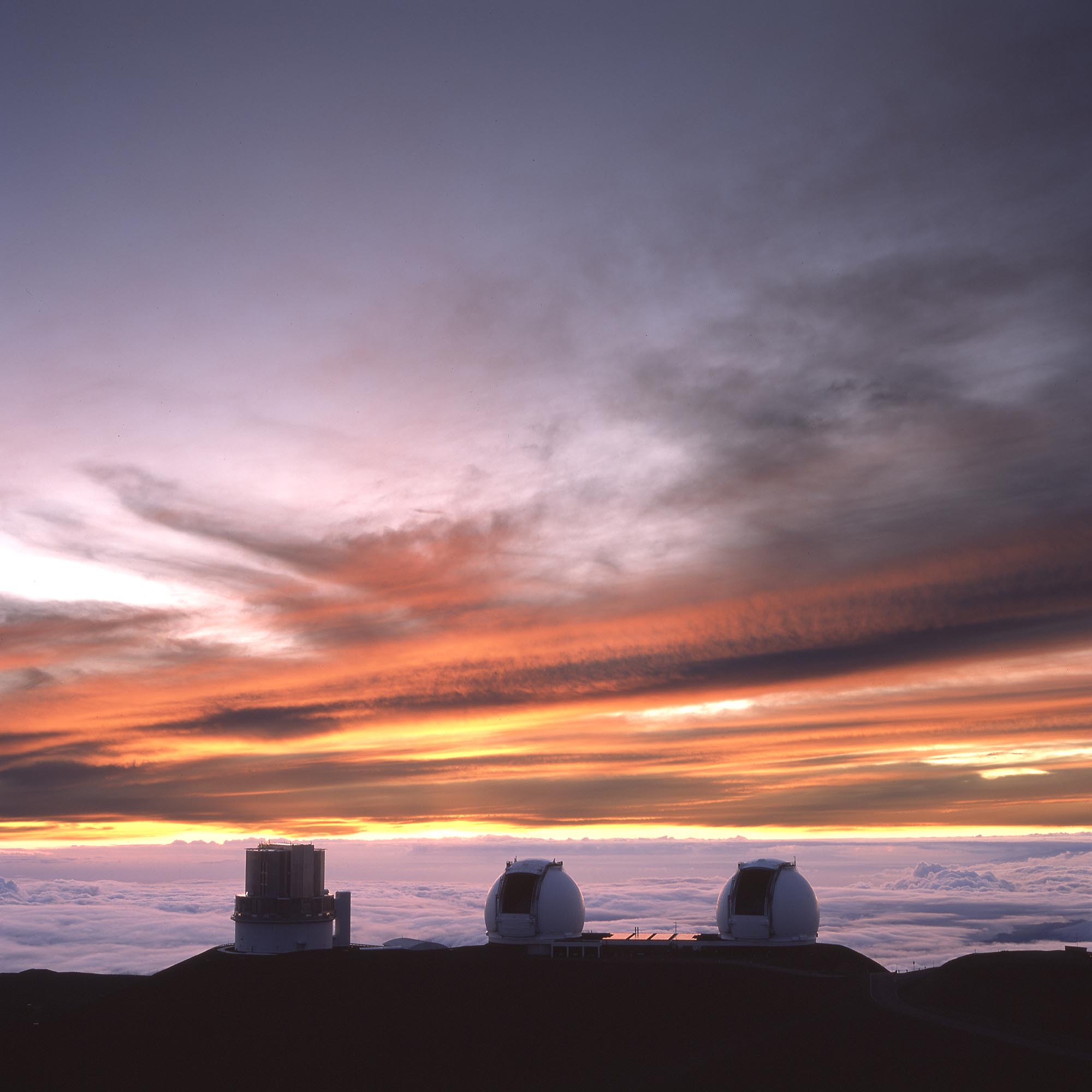 Three observatory buildings above the cloud layer at sunset