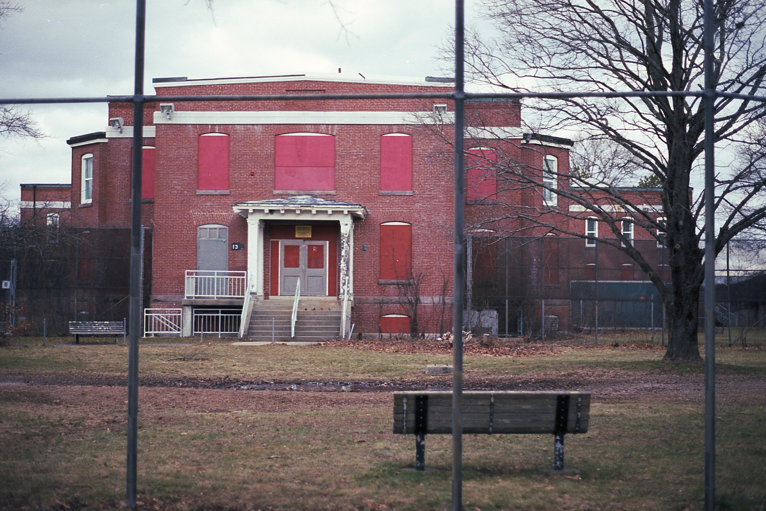 An abandoned hospital building through a chain link fence