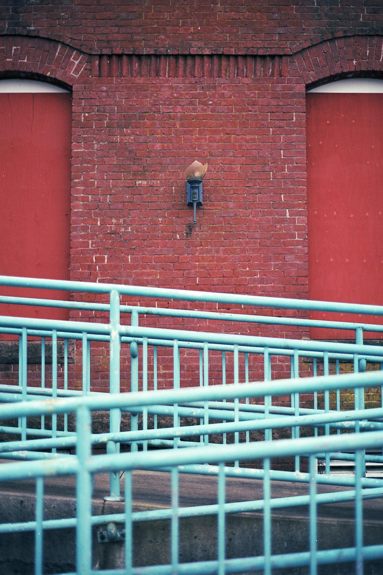 A switchback ramp with a bright blue railing in front of a red brick wall