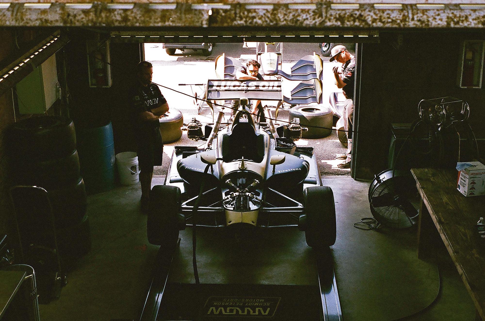 An IndyCar in the garage with three mechanics