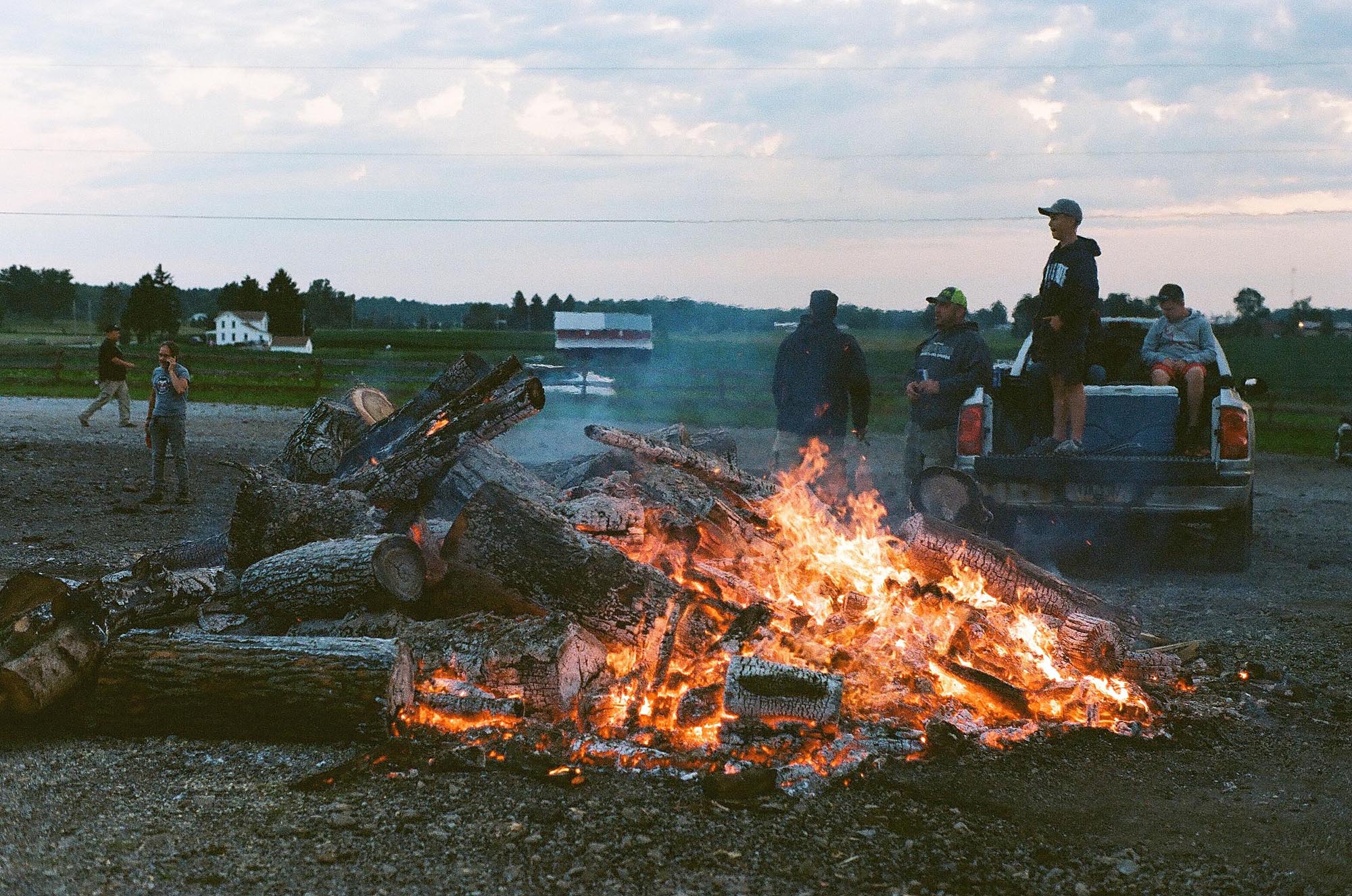 Four people in the back of a pickup truck near a bonfire