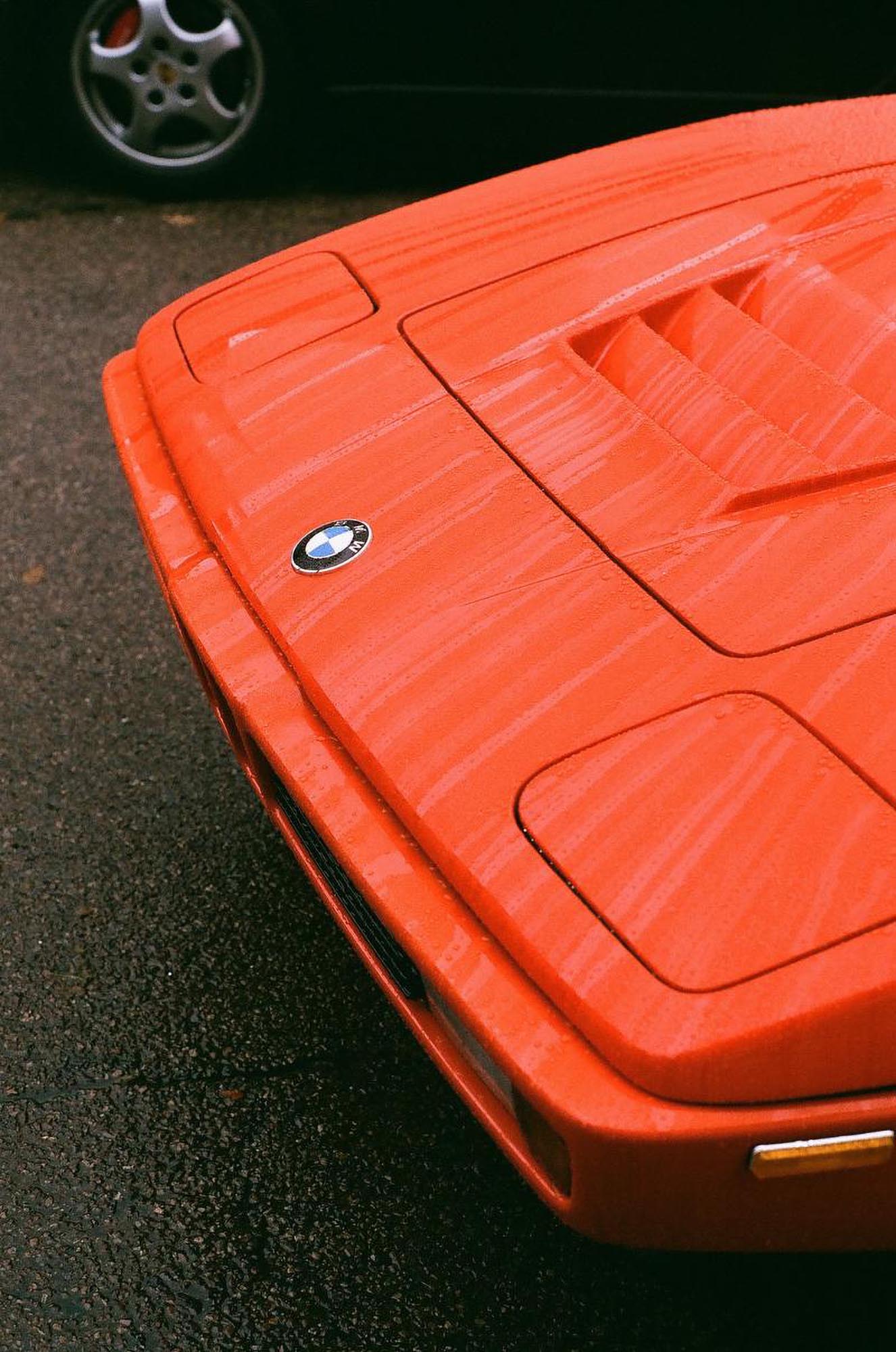 The front corner of a red BMW M1 in the rain