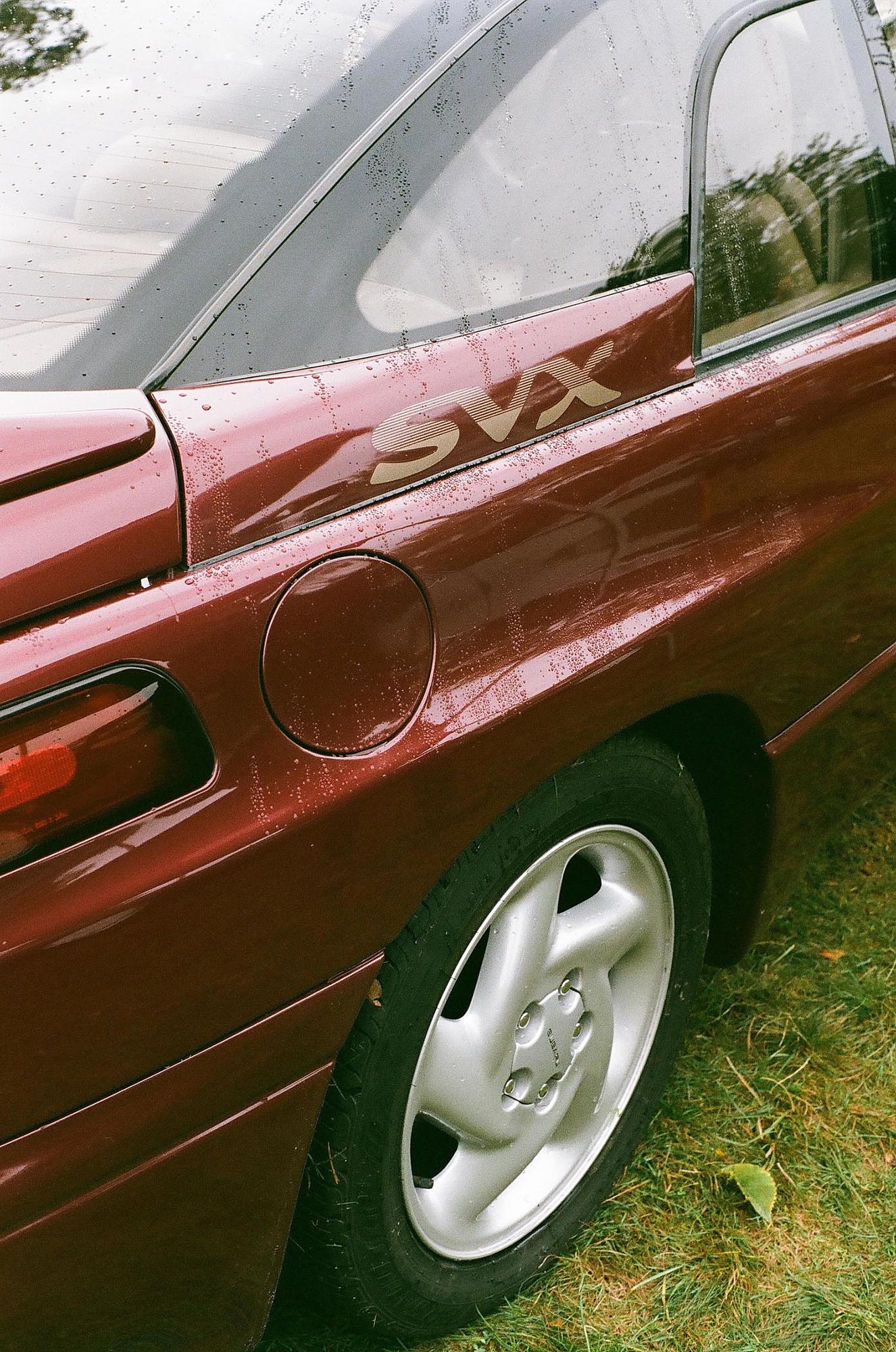 The rear corner of a maroon Subaru SVX