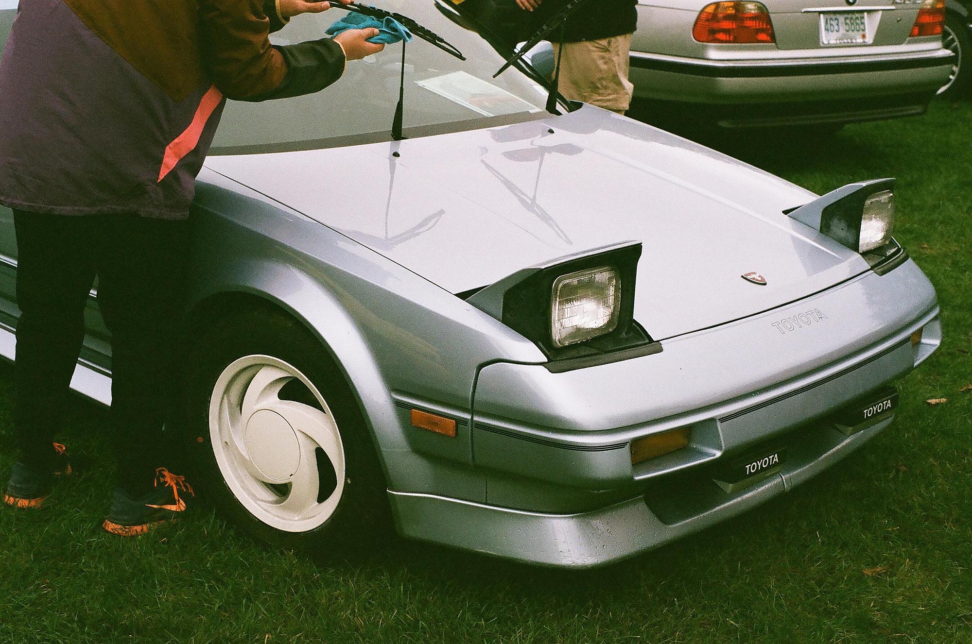 A person wiping the windshied wipers on a light blue Toyota MR2