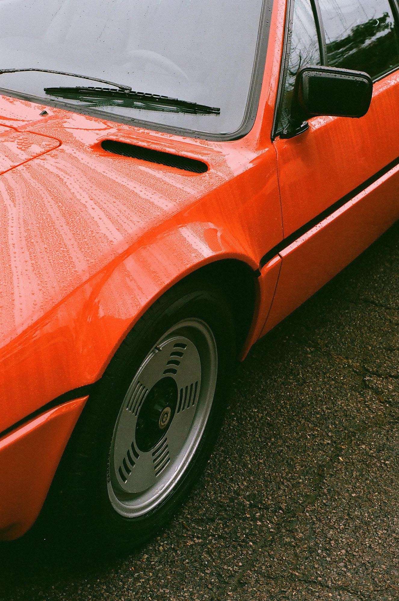 The front corner of a red BMW M1 in the rain