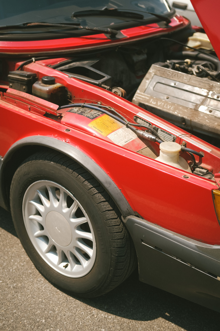 The front left wheel of a red Saab 900 with the hood up