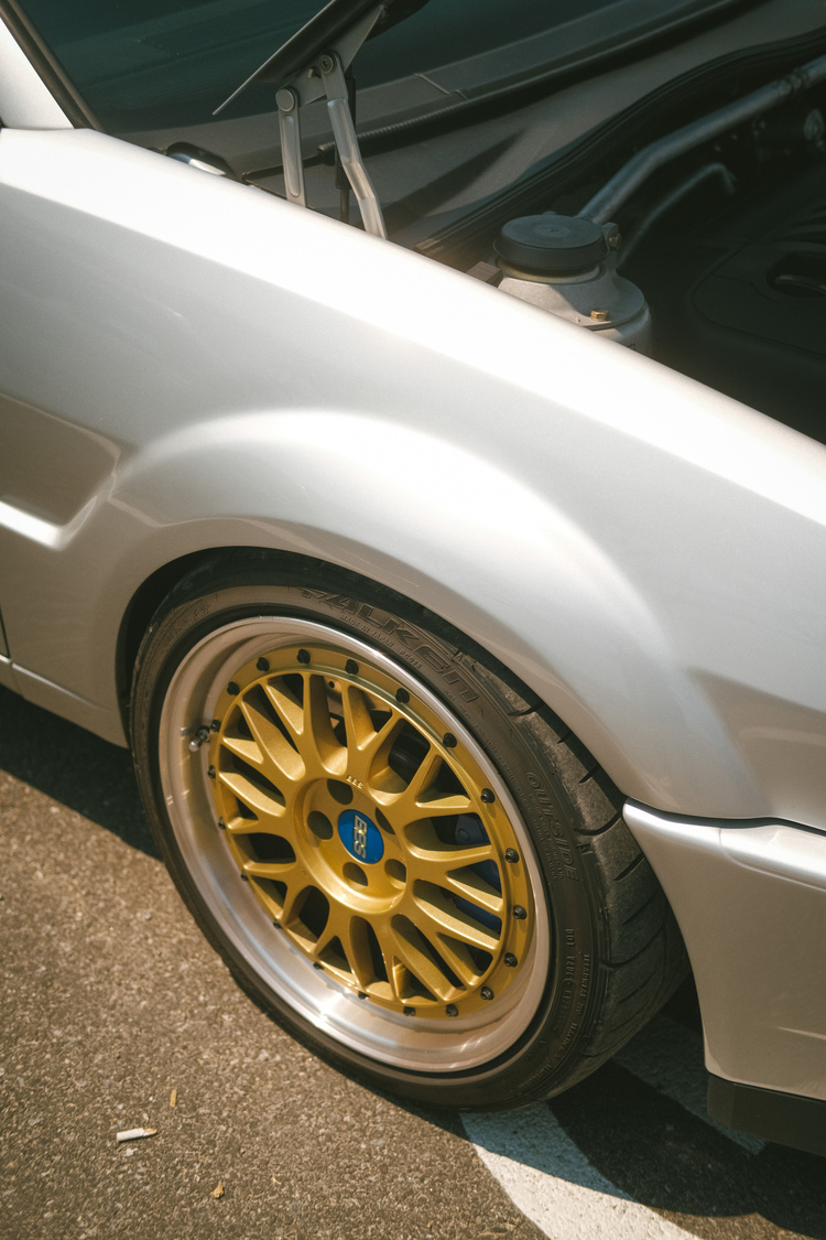 The golden front left wheel of a silver VW Scirocco with the hood up