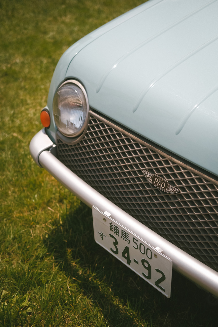 The front corner of a light blue Nissan Pao