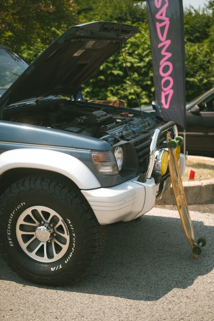 The front of a Mitsubishi SUV with a longboard leaned up against it