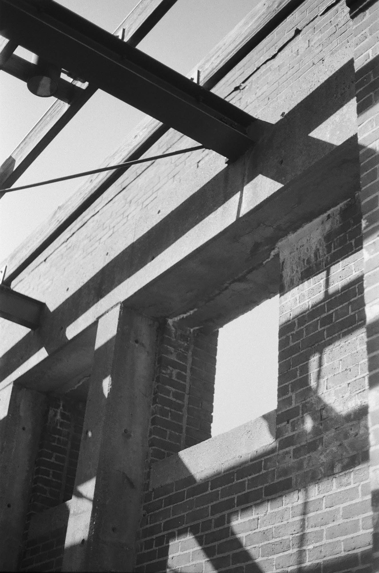An abstract picture of a brick and concrete wall with steel beams above, open to the sky