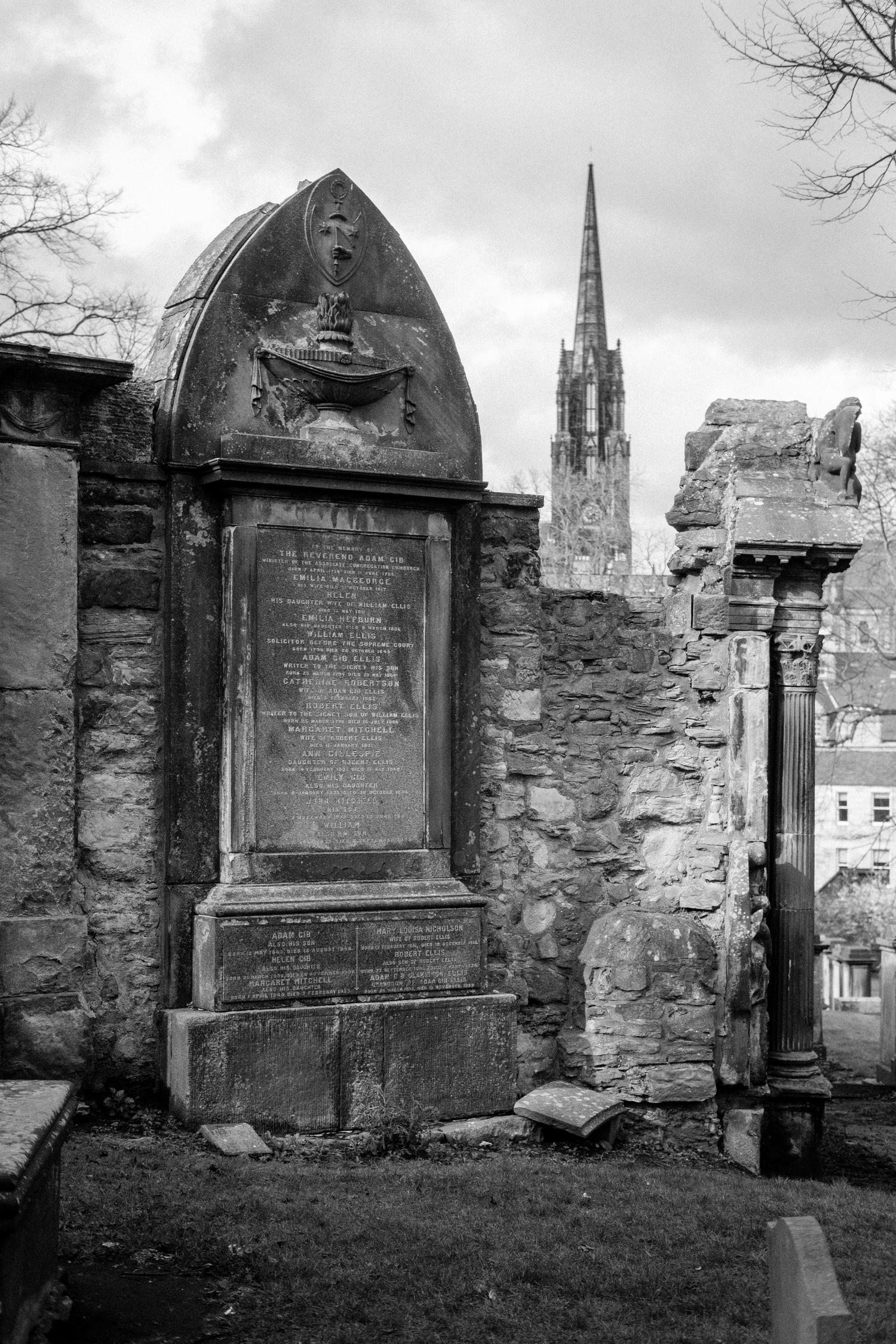 An old grave marker built into a stone wall with a church spire in the distance