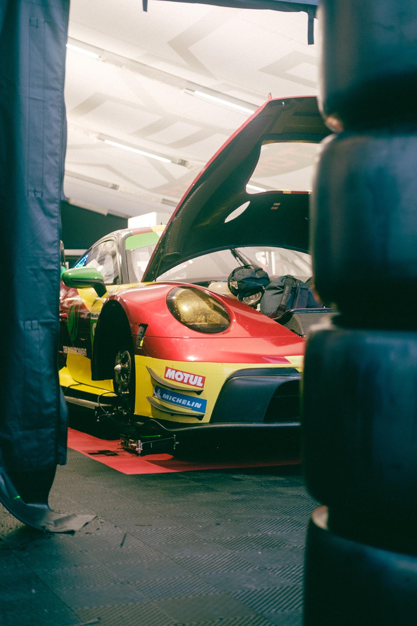 A Porsche 911 in the paddock seen through stacks of tires