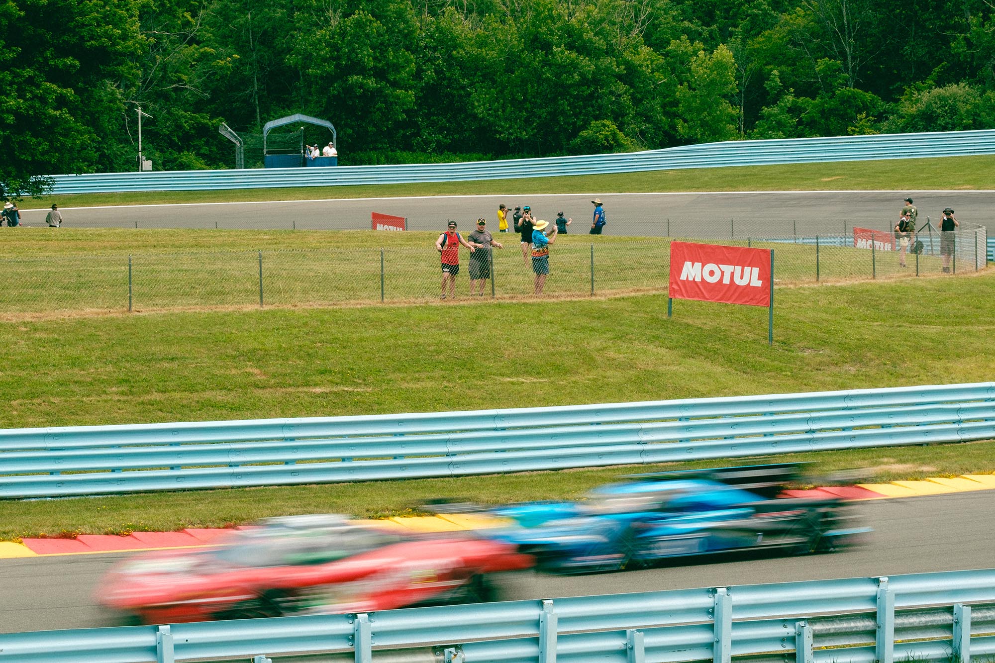 Two prototype cars blurred on track in front of a group of four spectators