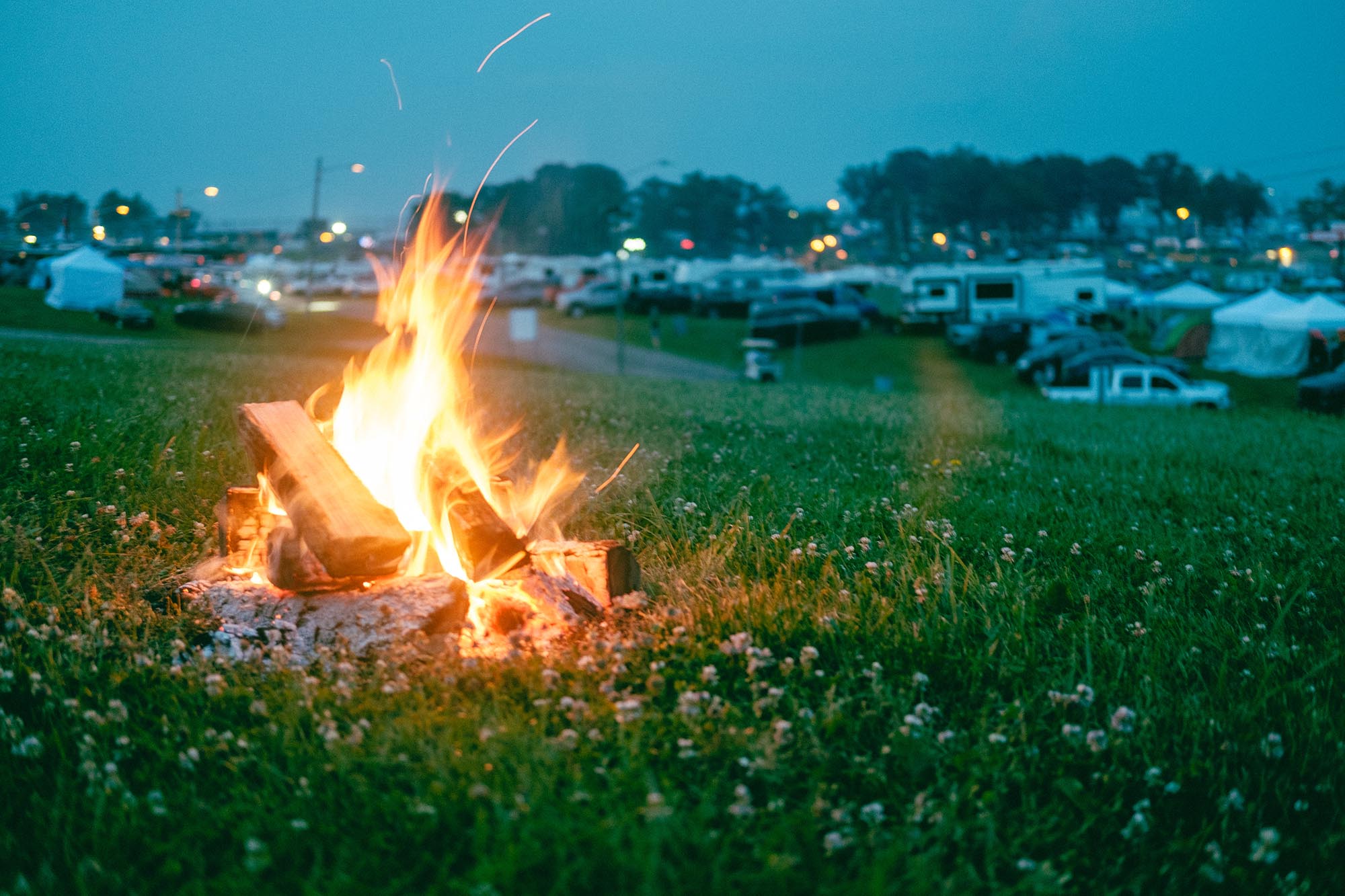 A campfire with RVs in the distance at dusk