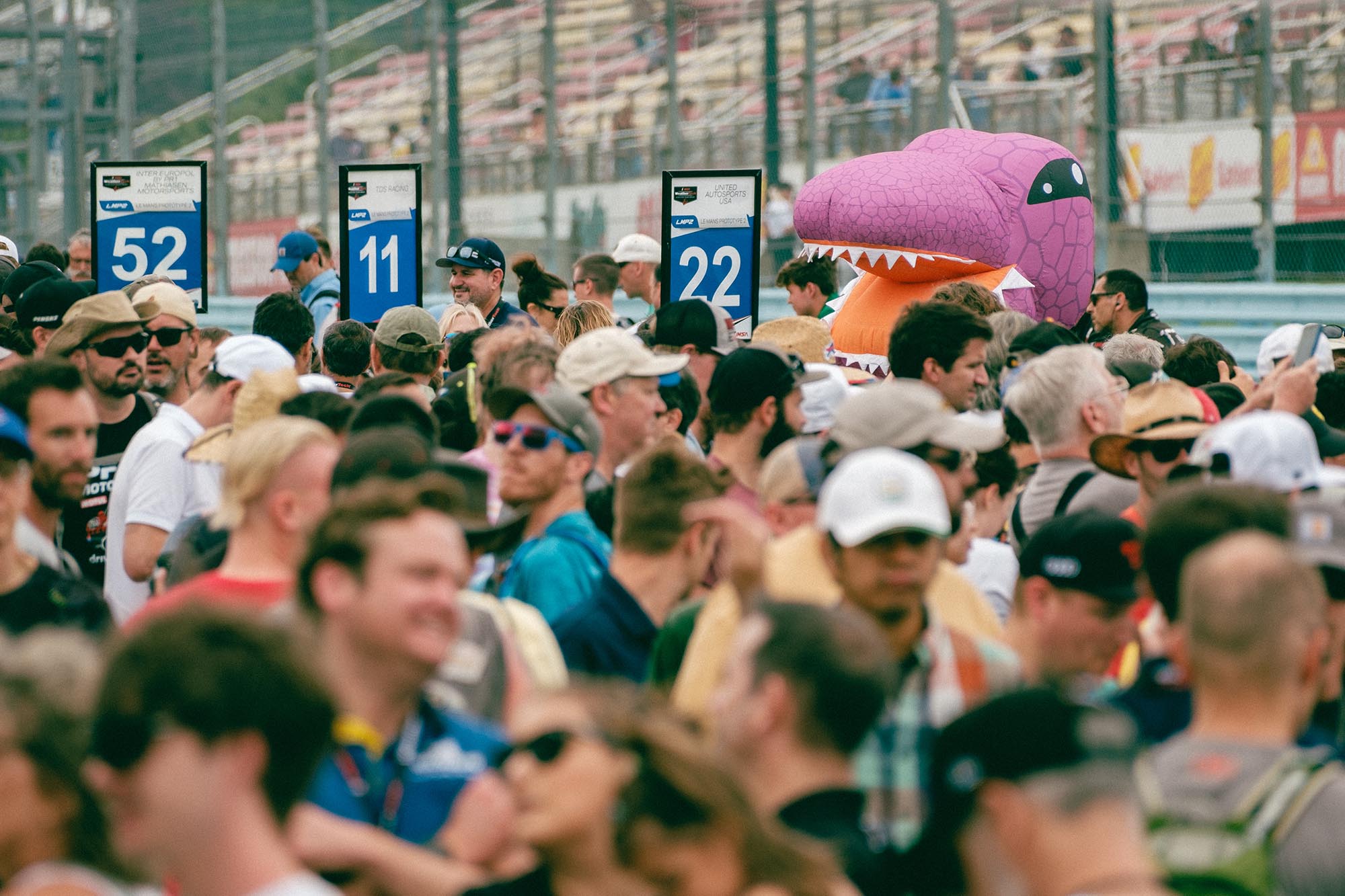 A crowd in pit lane with an inflatable dinosaur peeking above