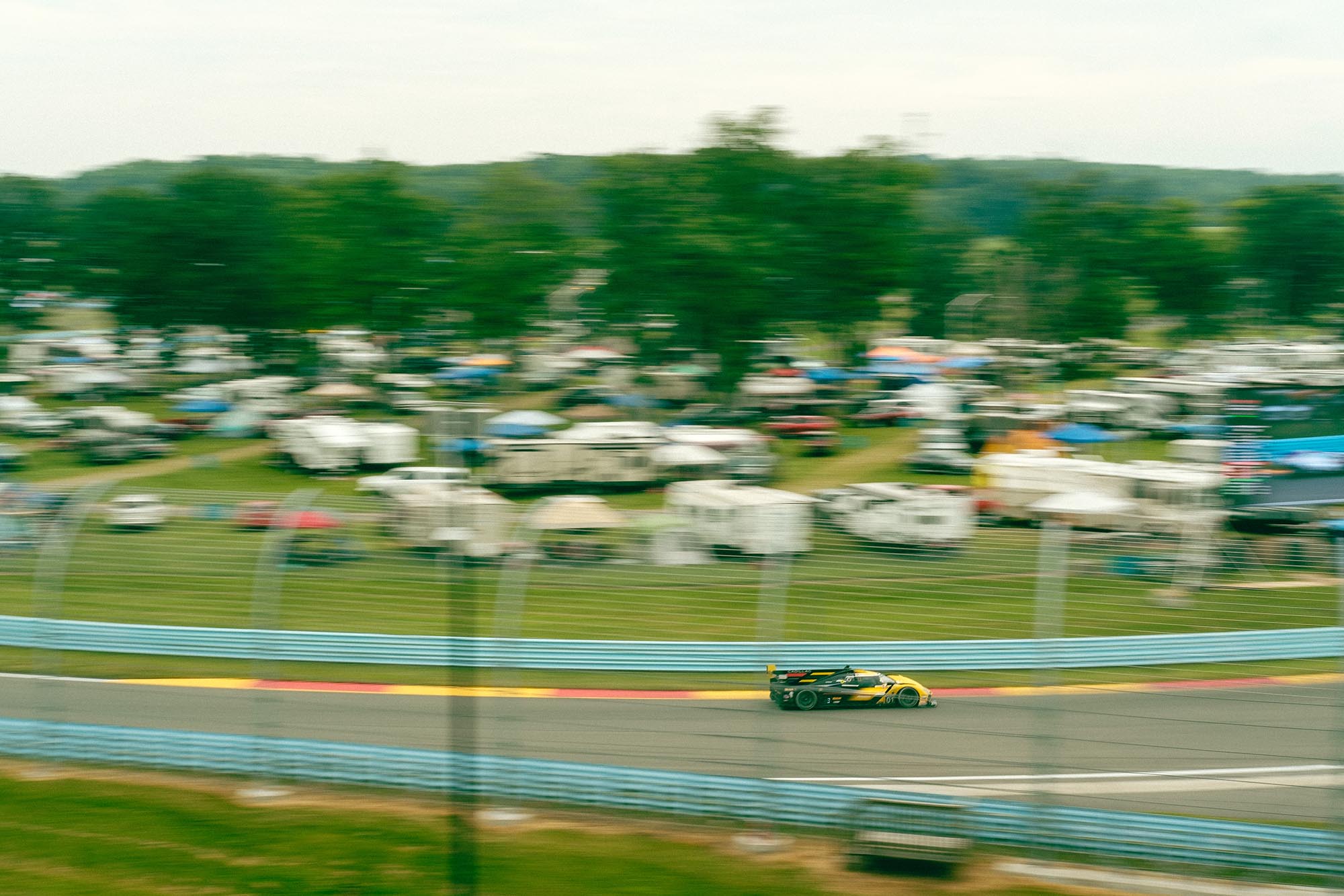 A Cadillac prototype on track with campgrounds in the distance