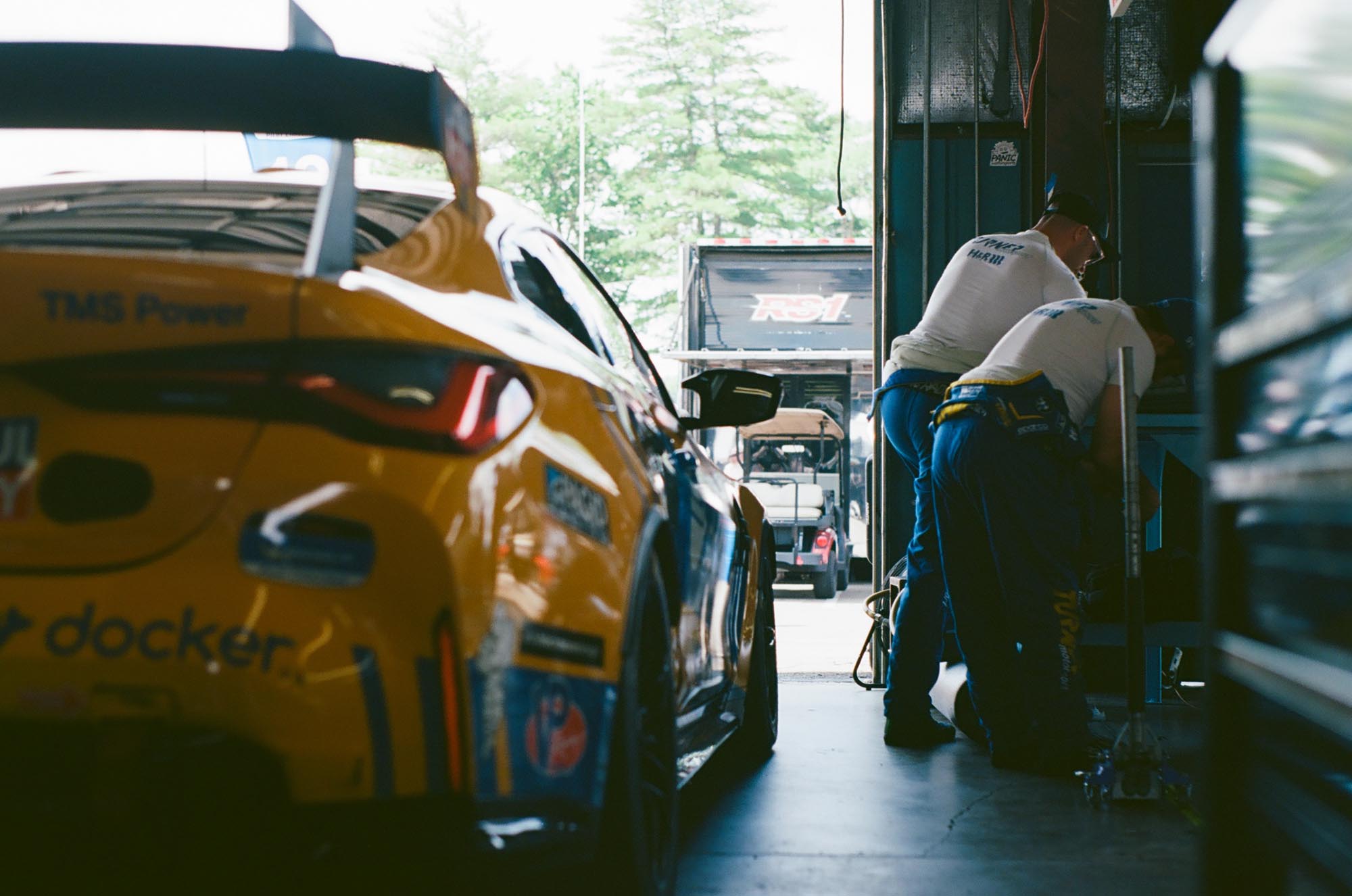 Two pit crew members near a blue and yellow BMW race car