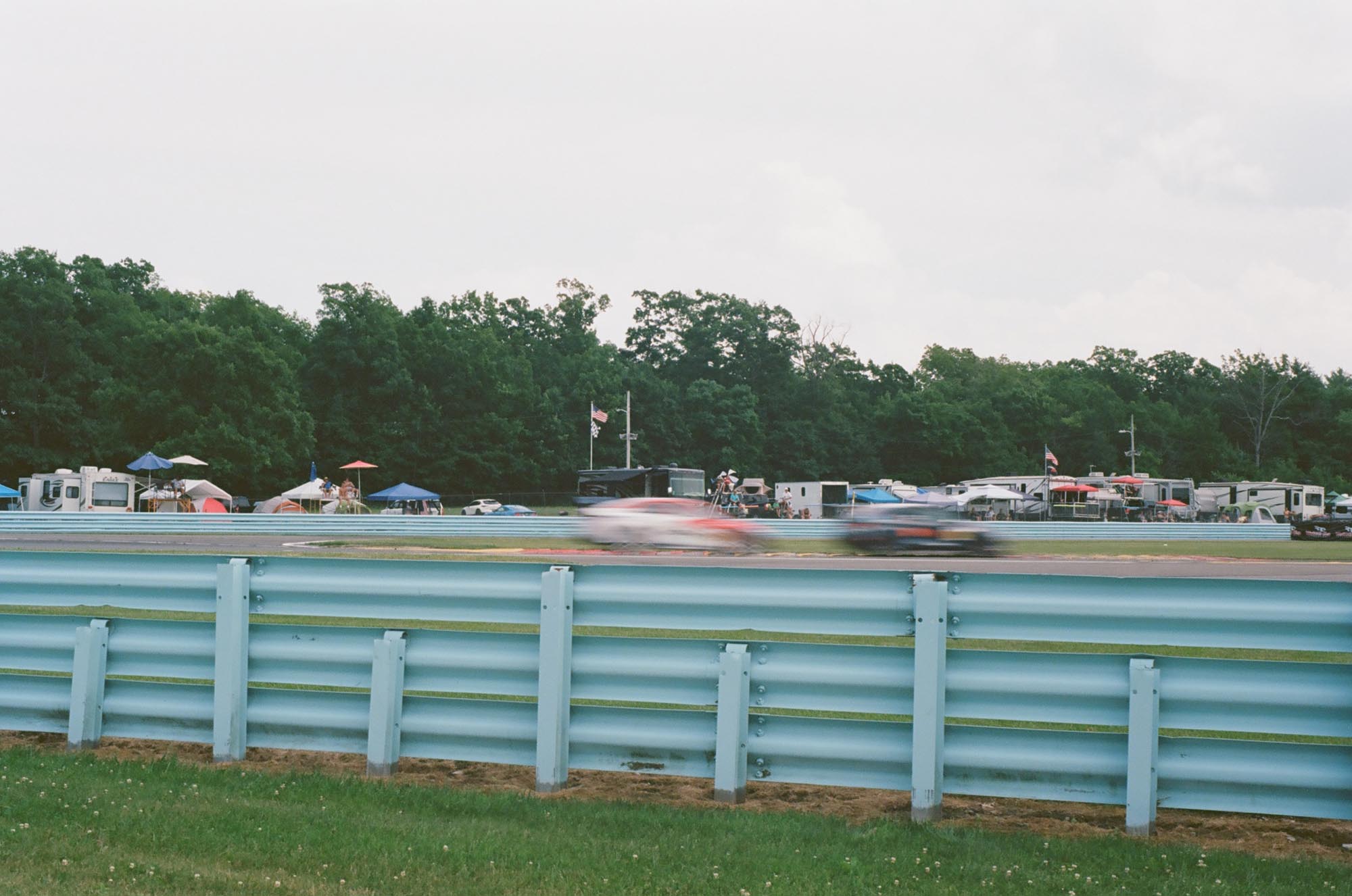 Blurred race cars on track with campers in the background